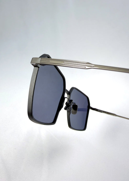 Close-up hinge detail view of Rigel sunglasses in Blue Graphite, featuring an ultra-light frame with titanium temples, geometric lens shape, and polarized lenses, showing the hinge construction and lens edge. 