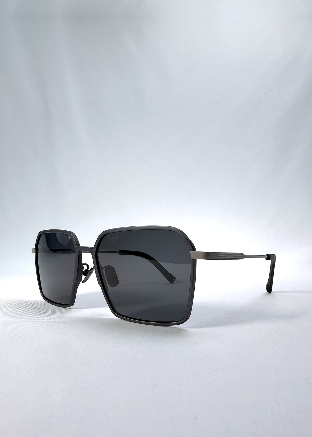 Three-quarter front view of Rigel sunglasses in Gunmetal Ash, featuring an ultra-light frame with titanium temples, geometric lens shape, and polarized lenses, showing the front shape and temple profile.