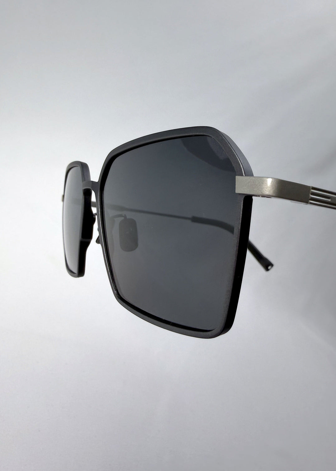 Close-up hinge detail view of Rigel sunglasses in Gunmetal Ash, featuring an ultra-light frame with titanium temples, geometric lens shape, and polarized lenses, showing the hinge construction and lens edge. 