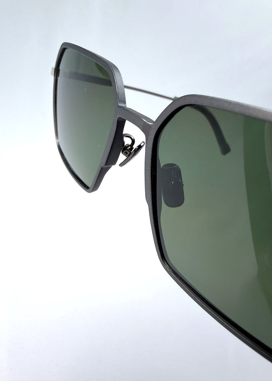 Close-up hinge detail view of Rigel sunglasses in Olive Smoke, featuring an ultra-light frame with titanium temples, geometric lens shape, and polarized lenses, showing the hinge construction and lens edge. 
