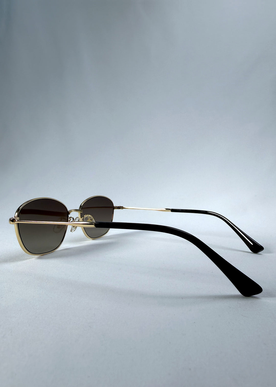 Back-angle view of Selene Line sunglasses in Amber Gold, featuring a slim gold-tone oval metal frame and amber gradient lenses, showing the rear frame structure and temple alignment.