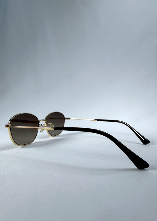 Back-angle view of Selene Line sunglasses in Amber Gold, featuring a slim gold-tone oval metal frame and amber gradient lenses, showing the rear frame structure and temple alignment.