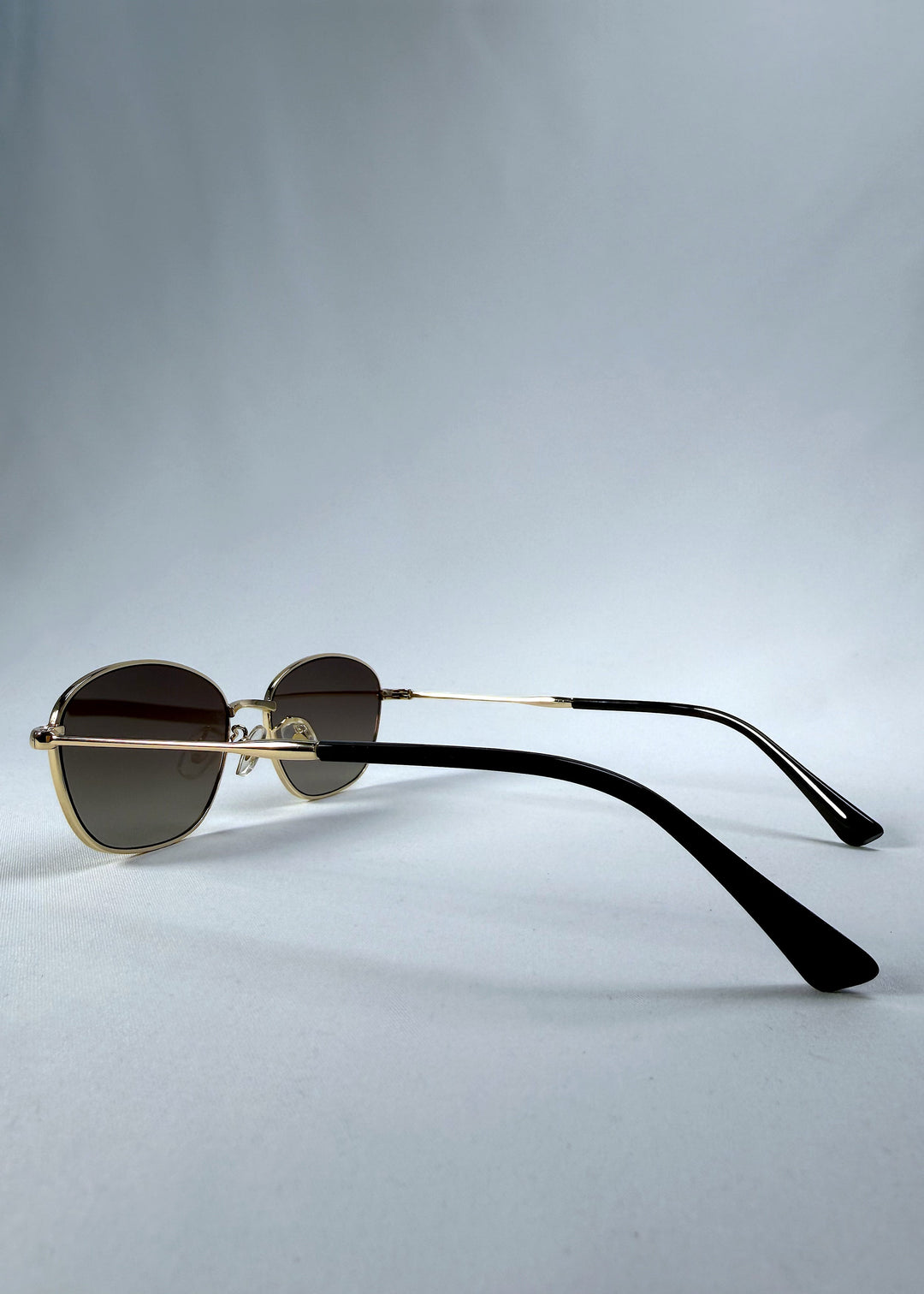 Back-angle view of Selene Line sunglasses in Amber Gold, featuring a slim gold-tone oval metal frame and amber gradient lenses, showing the rear frame structure and temple alignment. 