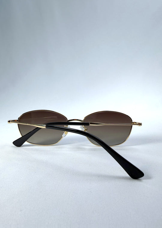 Folded back view of Selene Line sunglasses in Amber Gold, featuring a slim gold-tone oval metal frame and amber gradient lenses, showing the rear frame and crossed folded temples.