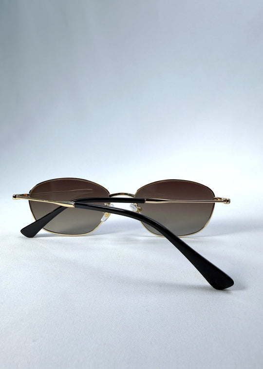 Folded back view of Selene Line sunglasses in Amber Gold, featuring a slim gold-tone oval metal frame and amber gradient lenses, showing the rear frame and crossed folded temples. 