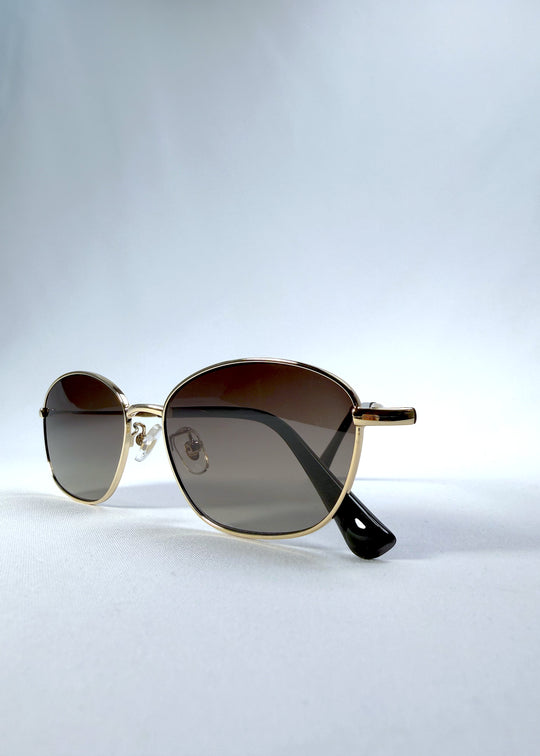 Folded front view of Selene Line sunglasses in Amber Gold, featuring a slim gold-tone oval metal frame and amber gradient lenses, showing the front frame and folded temples.