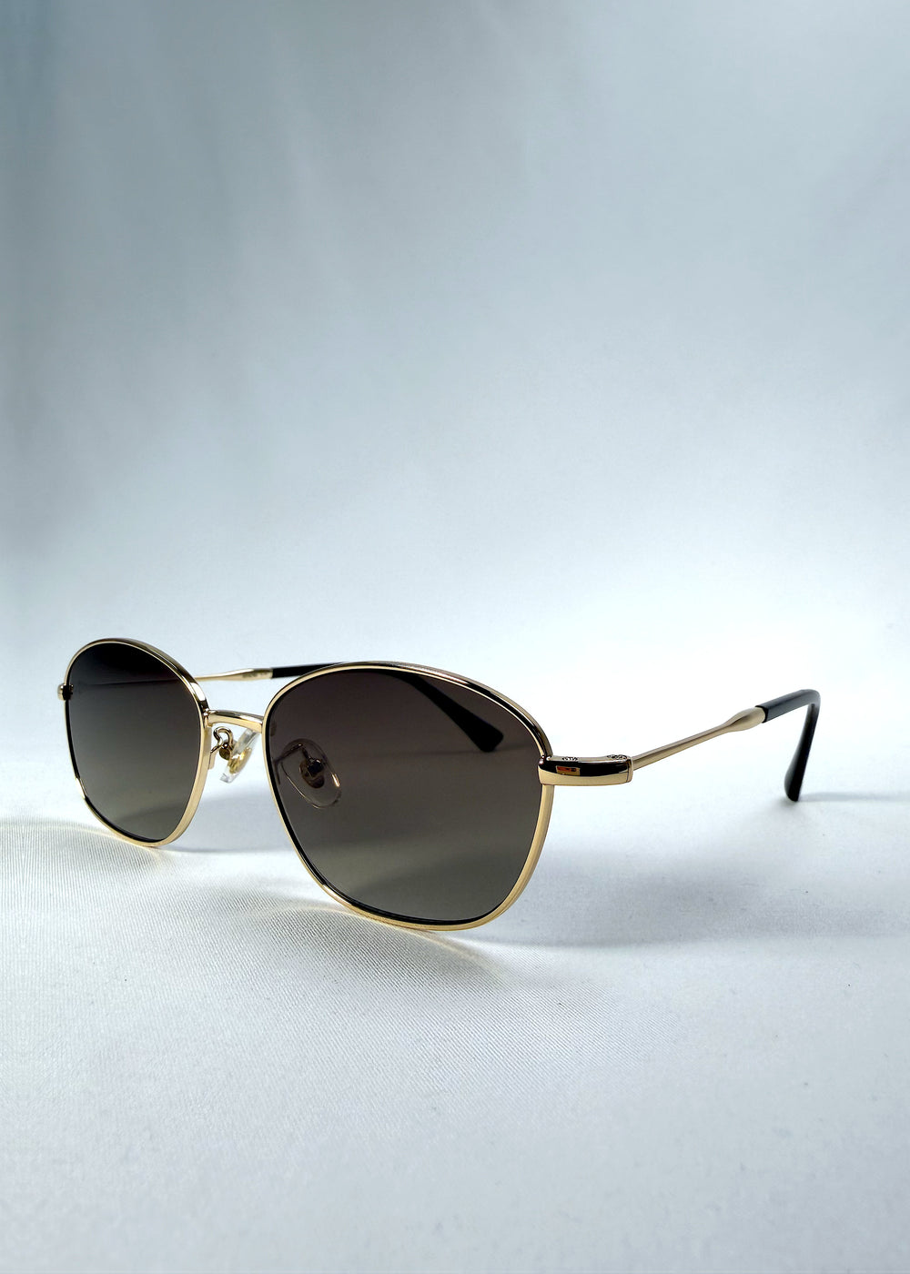 Three-quarter front view of Selene Line sunglasses in Amber Gold, featuring a slim gold-tone oval metal frame and amber gradient lenses, showing the frame shape and temple profile.