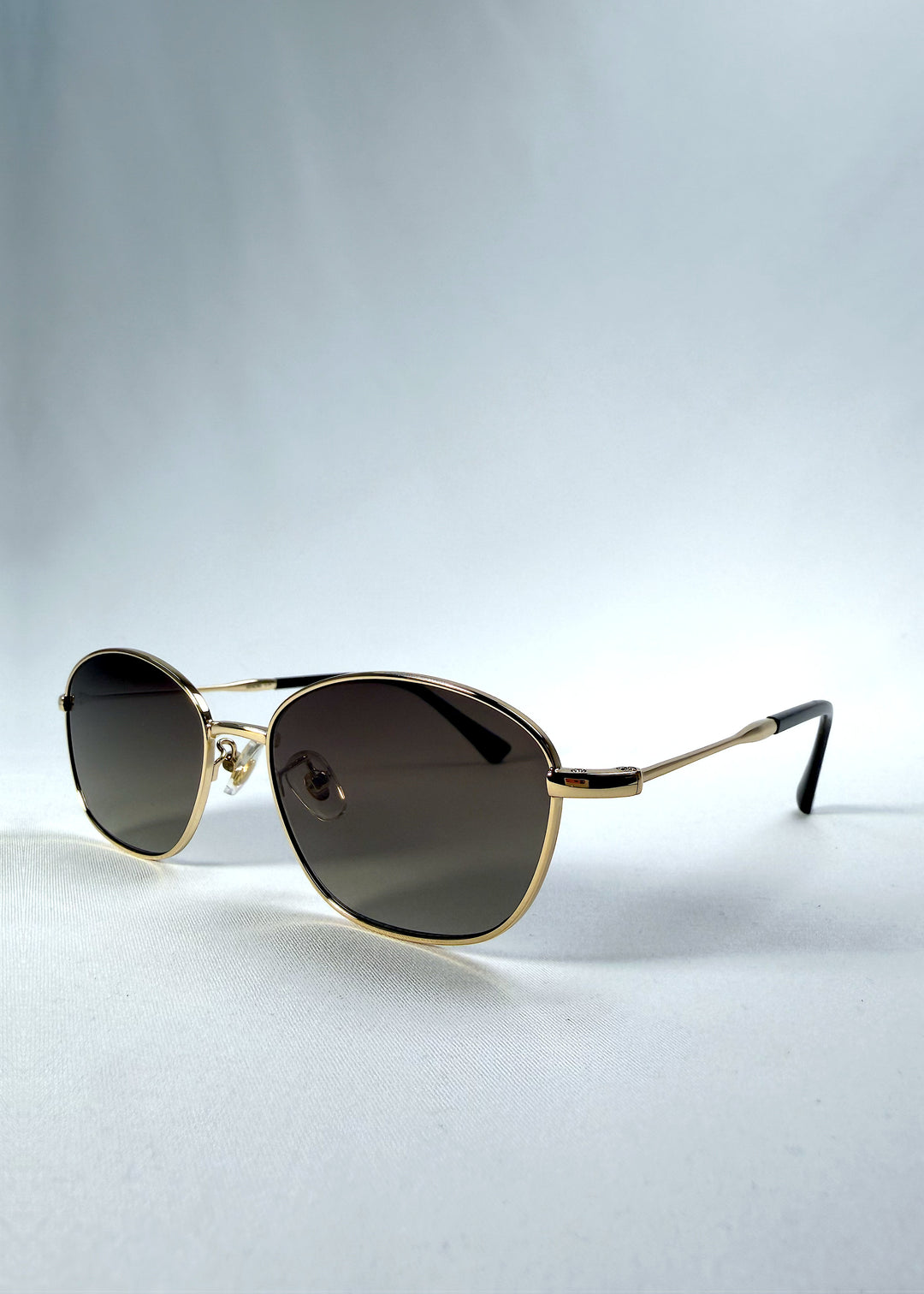 Three-quarter front view of Selene Line sunglasses in Amber Gold, featuring a slim gold-tone oval metal frame and amber gradient lenses, showing the frame shape and temple profile.
