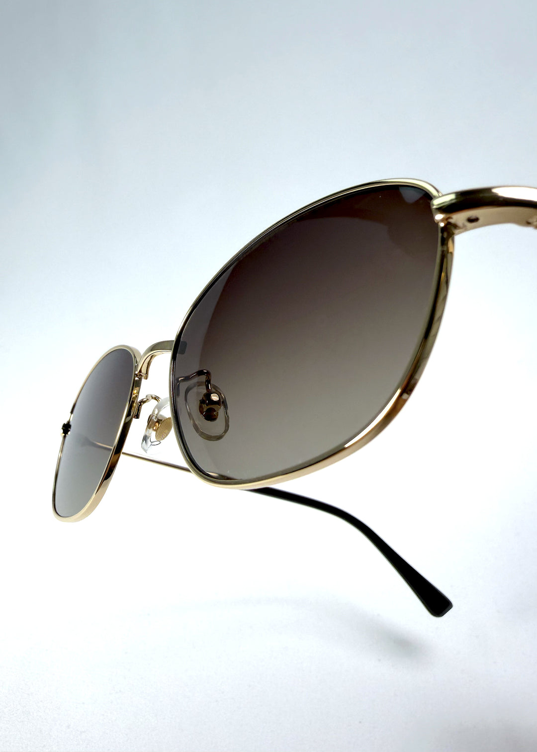Close-up hinge detail view of Selene Line sunglasses in Amber Gold, featuring a slim gold-tone oval metal frame and amber gradient lenses, showing the hinge construction, lens edge, and temple connection.