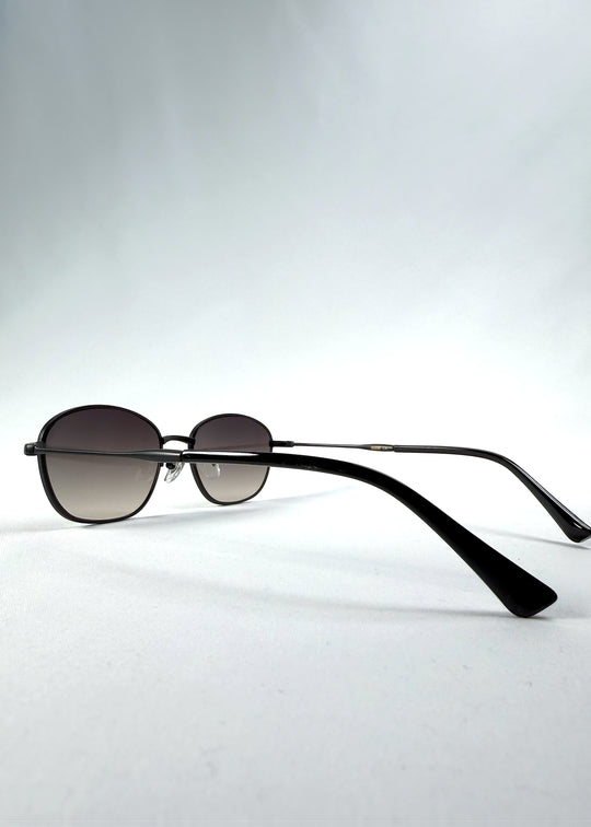 Back-angle view of Selene Line sunglasses in Matte Black, featuring a slim matte black oval metal frame and smoky gradient lenses, showing the rear frame structure and temple alignment.