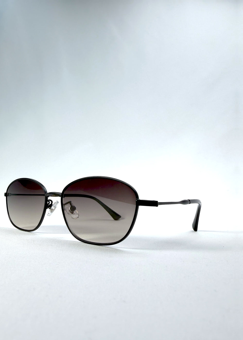 Three-quarter front view of Selene Line sunglasses in Matte Black, featuring a slim matte black oval metal frame and smoky gradient lenses, showing the frame shape and temple profile.