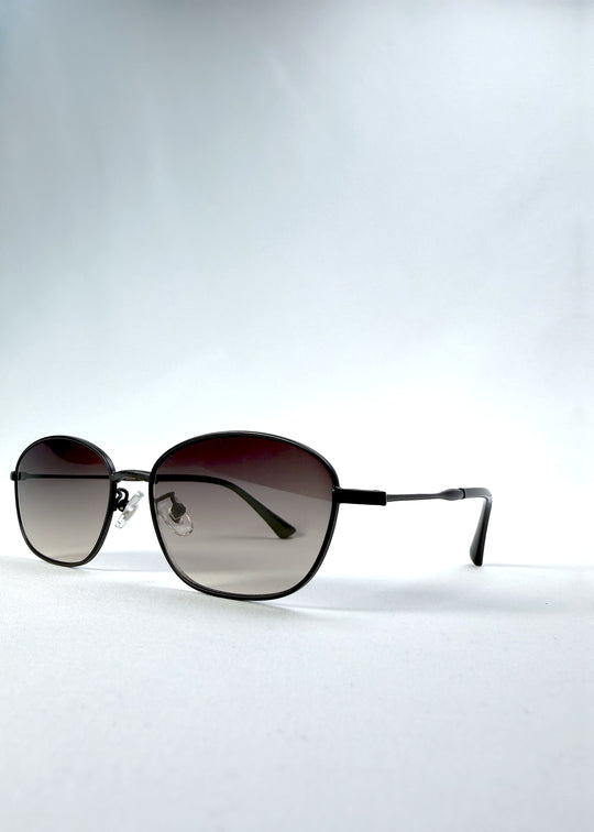 Three-quarter front view of Selene Line sunglasses in Matte Black, featuring a slim matte black oval metal frame and smoky gradient lenses, showing the frame shape and temple profile.