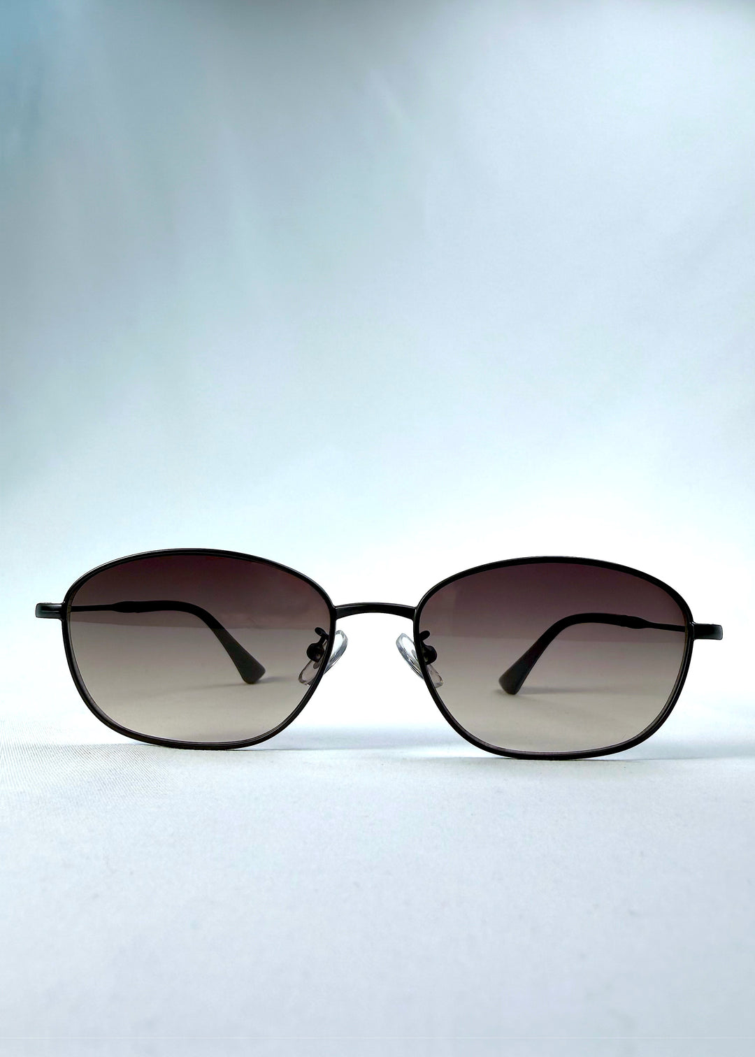 Front view of Selene Line sunglasses in Matte Black, featuring a slim matte black oval metal frame and smoky gradient lenses, showing the full front silhouette.