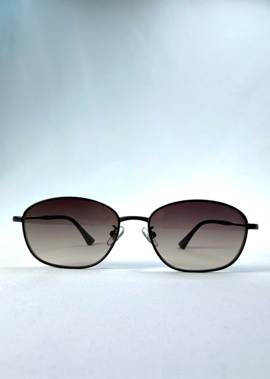 Front view of Selene Line sunglasses in Matte Black, featuring a slim matte black oval metal frame and smoky gradient lenses, showing the full front silhouette. 