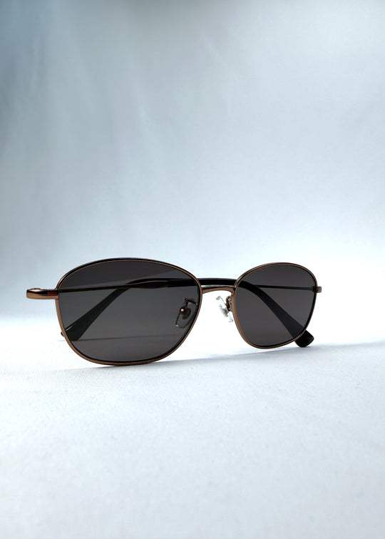 Folded view of AZE Selene Line sunglasses in Mocha Alloy, featuring a slim bronze-tone oval metal frame and smoky brown lenses, showing the folded temples and frame profile.
