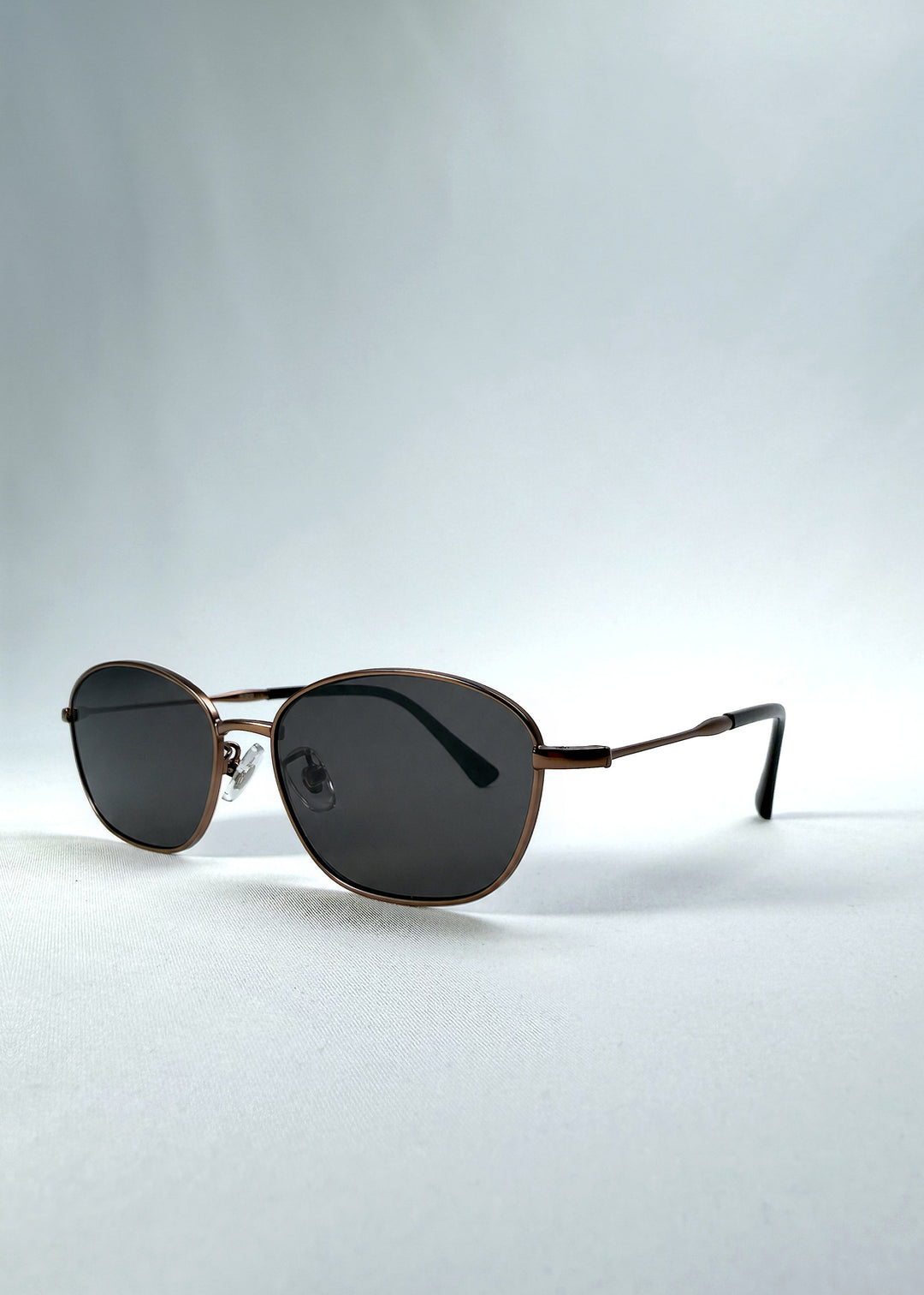 Three-quarter front view of AZE Selene Line sunglasses in Mocha Alloy, featuring a slim bronze-tone oval metal frame and smoky brown lenses, showing the frame shape and temple profile.