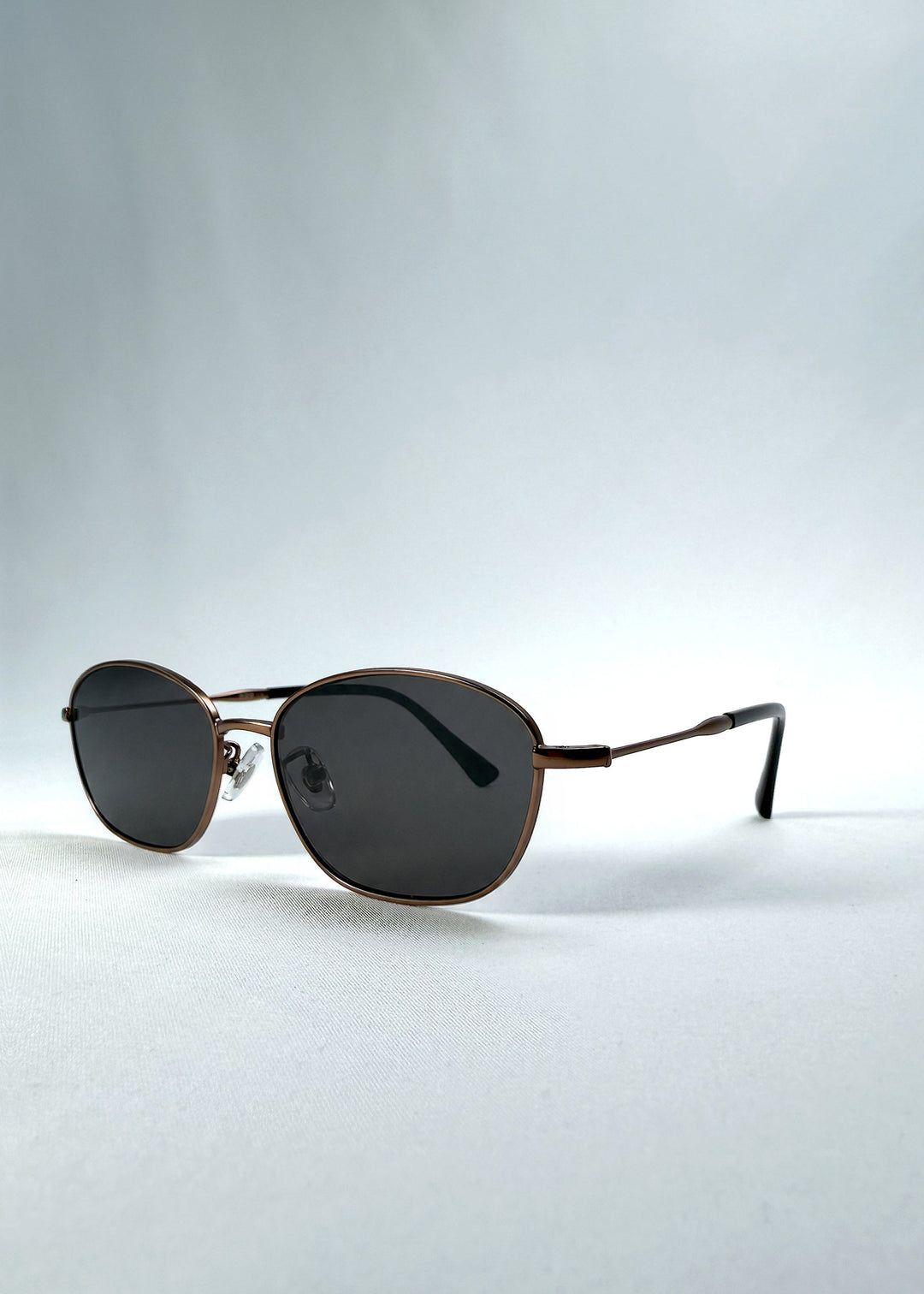 Three-quarter front view of AZE Selene Line sunglasses in Mocha Alloy, featuring a slim bronze-tone oval metal frame and smoky brown lenses, showing the frame shape and temple profile. 