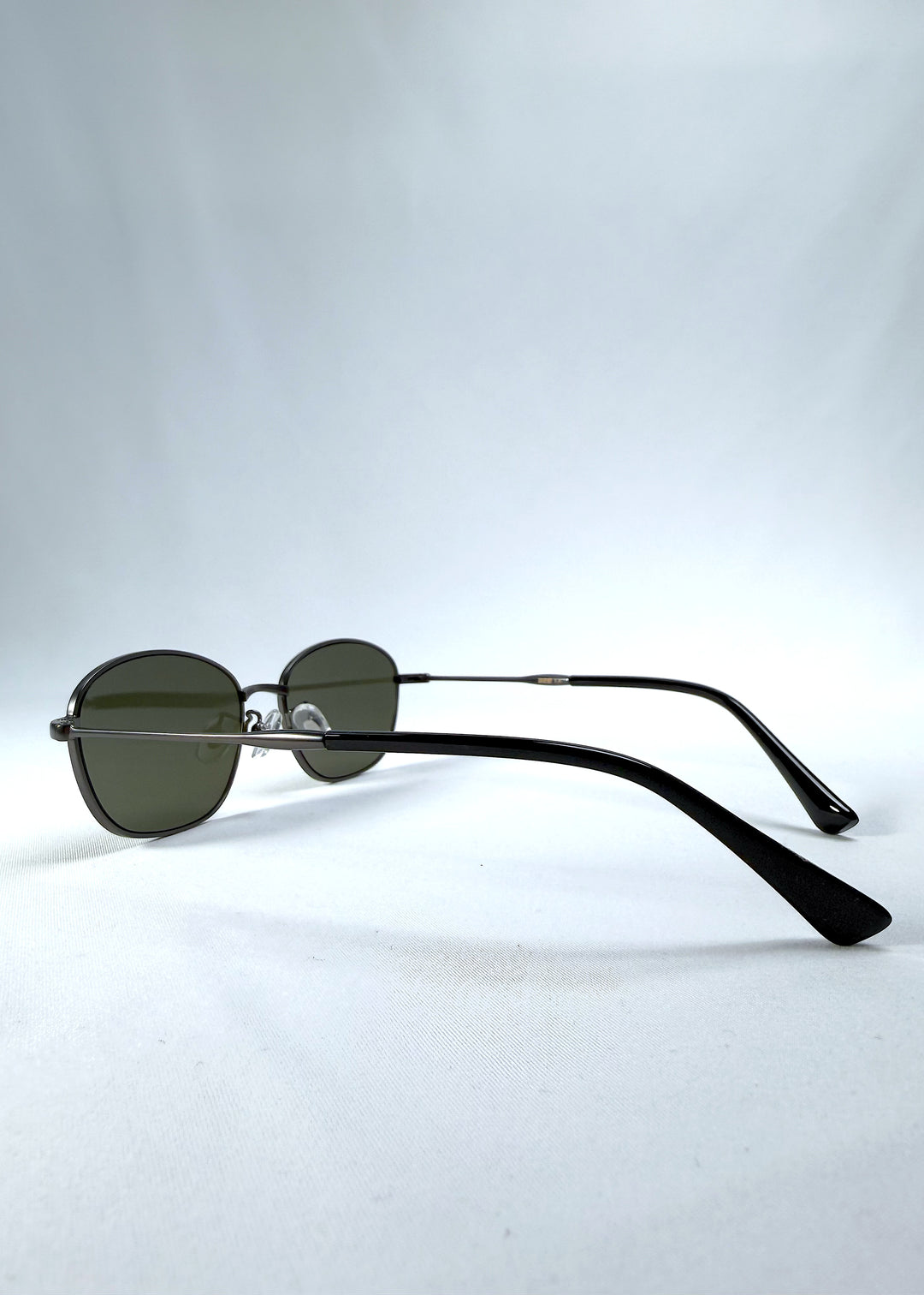 Back-angle view of AZE Selene Line sunglasses in Sage Gunmetal, featuring a slim gunmetal oval metal frame and sage-green lenses, showing the rear frame structure and temple alignment.