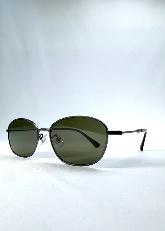 Three-quarter front view of AZE Selene Line sunglasses in Sage Gunmetal, featuring a slim gunmetal oval metal frame and sage-green lenses, showing the frame shape and temple profile. 