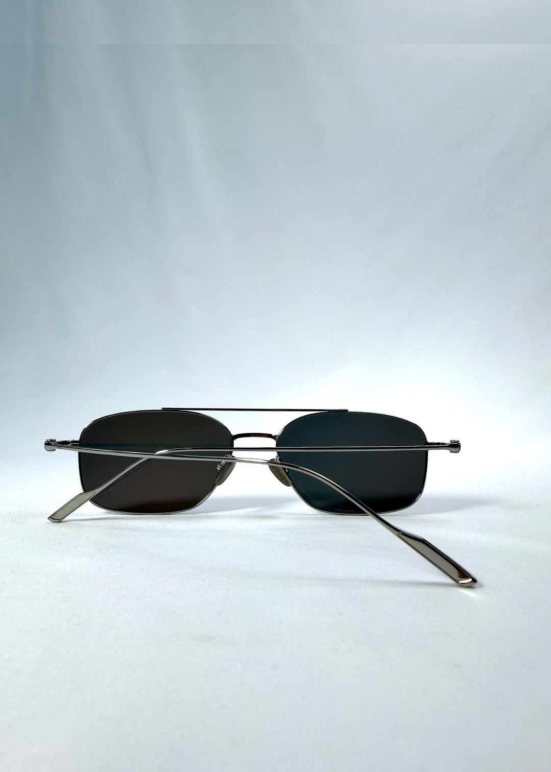 Folded back view of Seren Arc sunglasses in Gunmetal Veil, featuring gunmetal frame and dark tinted lenses, showing the folded temples and back structure. 