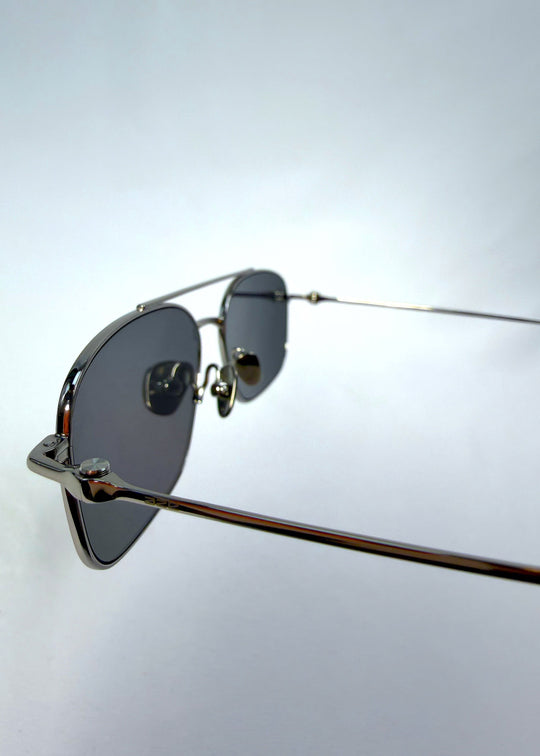 Close-up hinge detail view of Seren Arc sunglasses in Gunmetal Veil, featuring gunmetal frame and dark tinted lenses, showing the hinge, lens edge, and temple detail. 