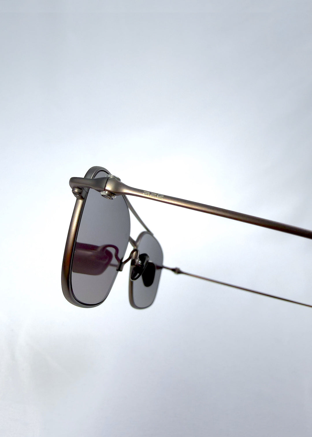 Close-up hinge detail view of Seren Arc sunglasses in Mocha Alloy, featuring mocha metal frame and rose-brown lenses, showing the hinge, lens edge, and temple detail. 