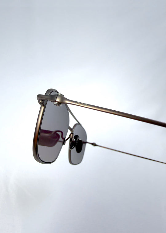 Close-up hinge detail view of Seren Arc sunglasses in Mocha Alloy, featuring mocha metal frame and rose-brown lenses, showing the hinge, lens edge, and temple detail. 