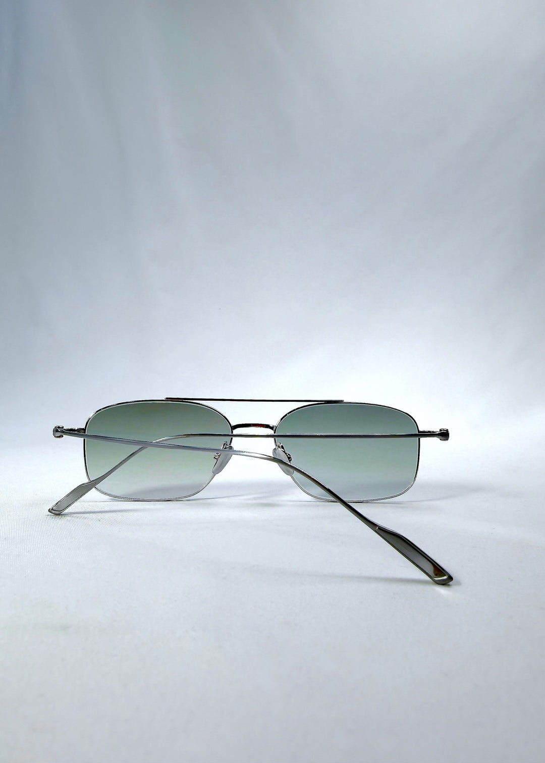 Folded back view of Seren Arc sunglasses in Moonlit Silver, featuring silver metal frame and pale green lenses, showing the folded temples and back structure. 