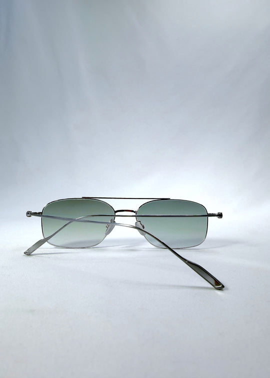 Folded back view of Seren Arc sunglasses in Moonlit Silver, featuring silver metal frame and pale green lenses, showing the folded temples and back structure. 