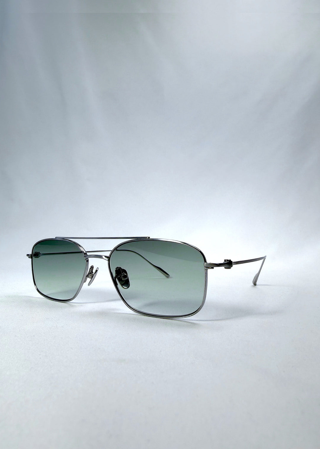 Three-quarter front view of Seren Arc sunglasses in Moonlit Silver, featuring silver metal frame and pale green lenses, showing the front shape and temple profile. 