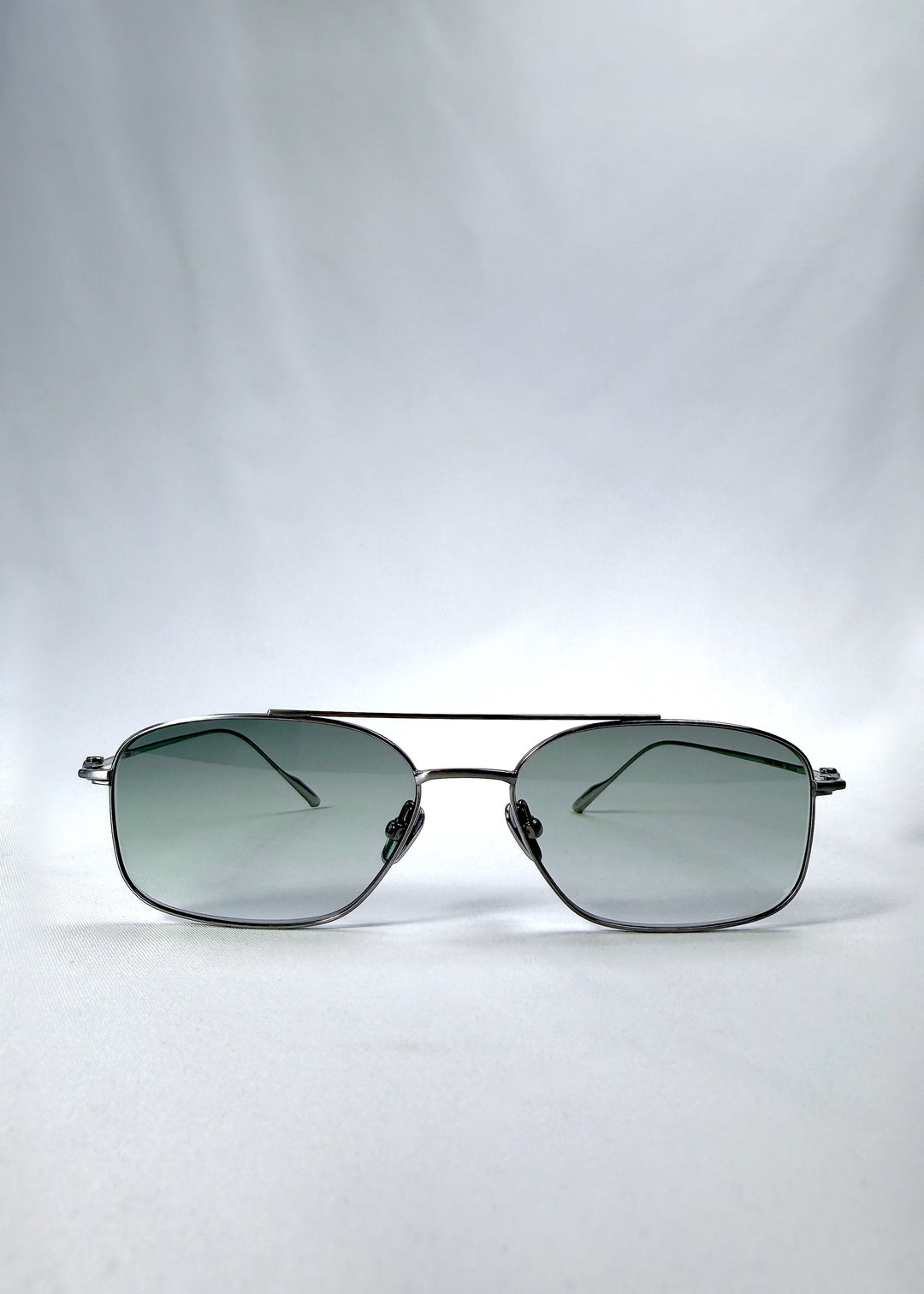Front view of Seren Arc sunglasses in Moonlit Silver, featuring silver metal frame and pale green lenses, showing the full front silhouette. 