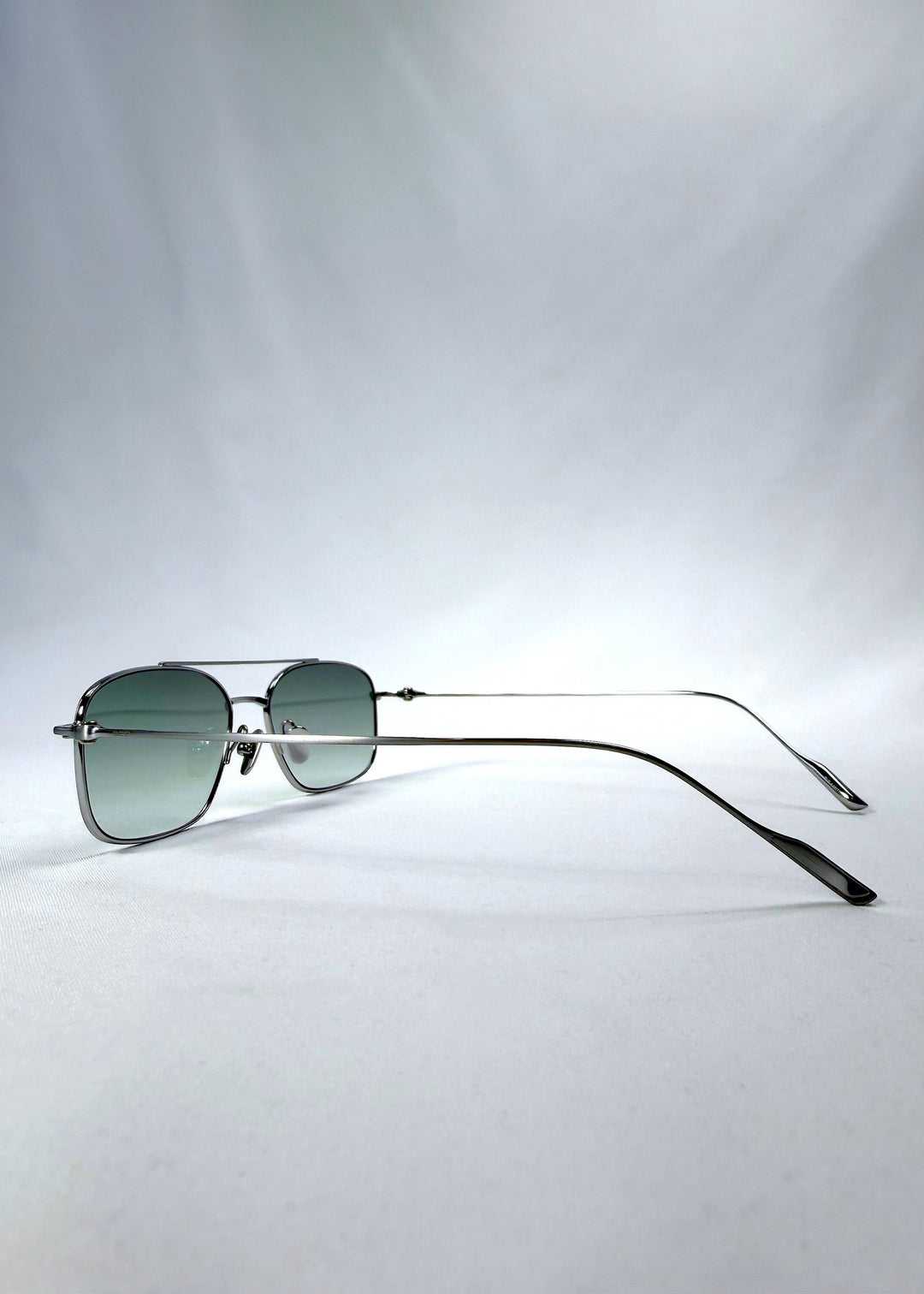 Side-angle view of Seren Arc sunglasses in Moonlit Silver, featuring silver metal frame and pale green lenses, showing the lens shape and side temple profile. 