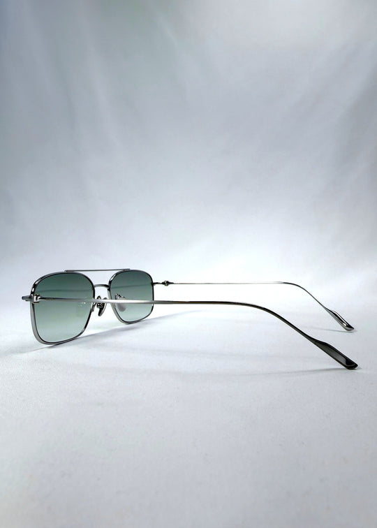 Side-angle view of Seren Arc sunglasses in Moonlit Silver, featuring silver metal frame and pale green lenses, showing the lens shape and side temple profile. 
