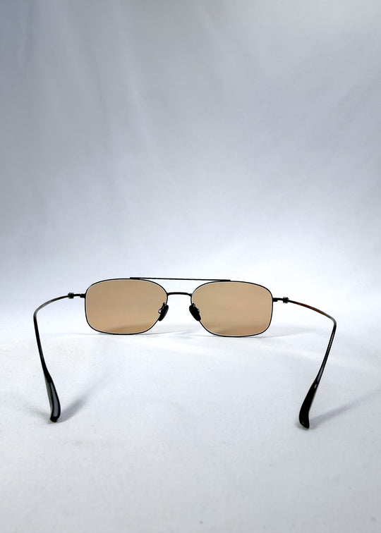 Back view of Seren Arc sunglasses in Obsidian Black, featuring black metal frame and warm brown lenses, showing the inside frame and open temples.