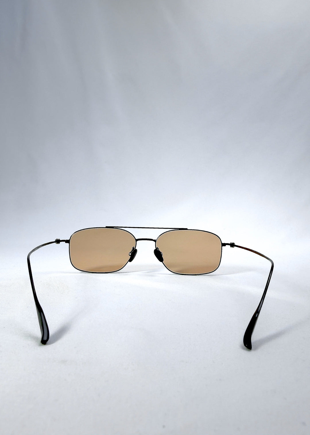 Back view of Seren Arc sunglasses in Obsidian Black, featuring black metal frame and warm brown lenses, showing the inside frame and open temples. 