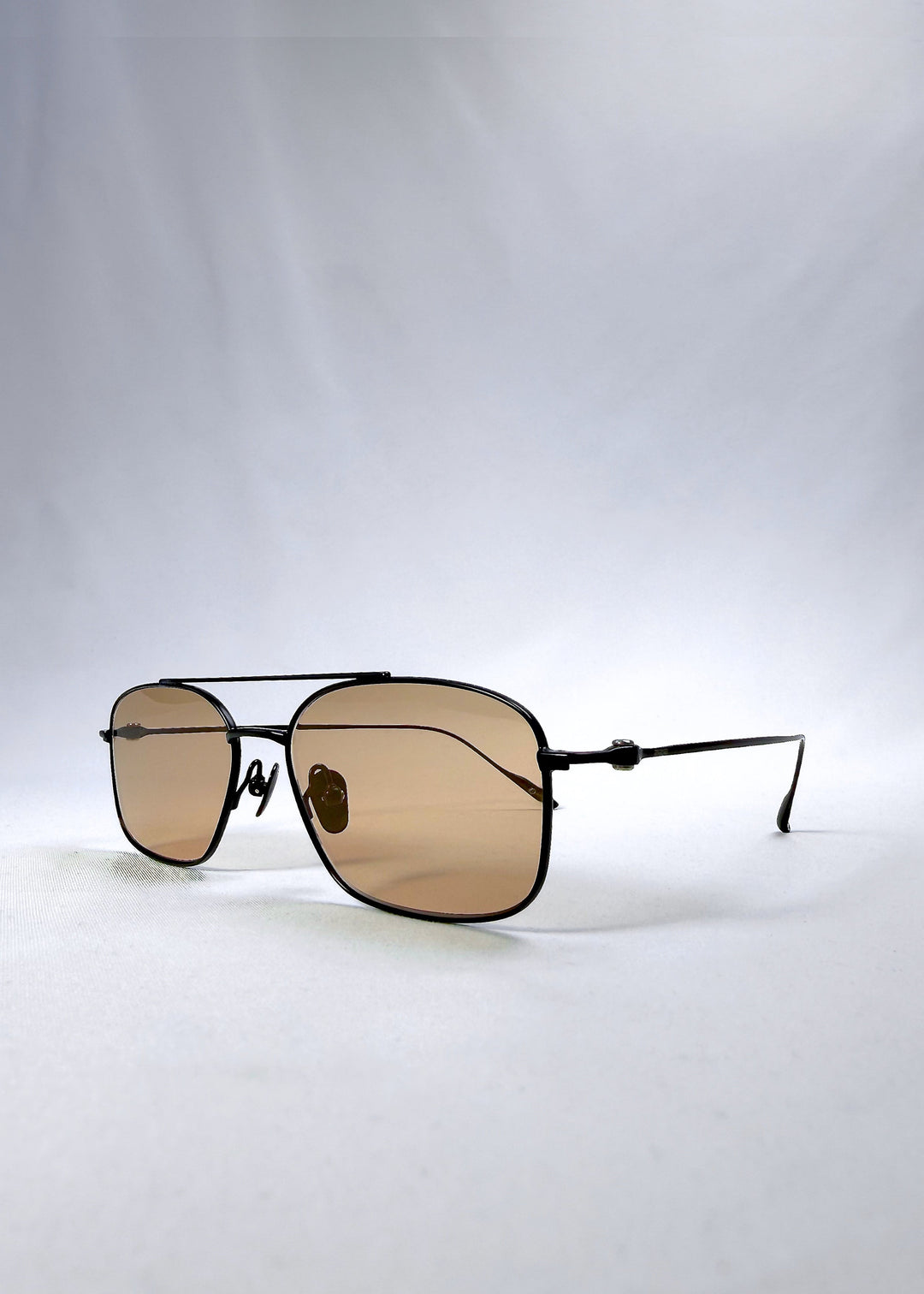 Three-quarter front view of Seren Arc sunglasses in Obsidian Black, featuring black metal frame and warm brown lenses, showing the front shape and temple profile. 