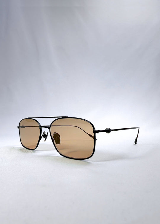 Three-quarter front view of Seren Arc sunglasses in Obsidian Black, featuring black metal frame and warm brown lenses, showing the front shape and temple profile. 