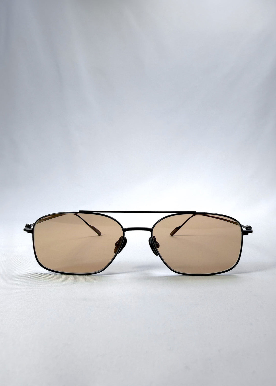 Front view of Seren Arc sunglasses in Obsidian Black, featuring black metal frame and warm brown lenses, showing the full front silhouette. 