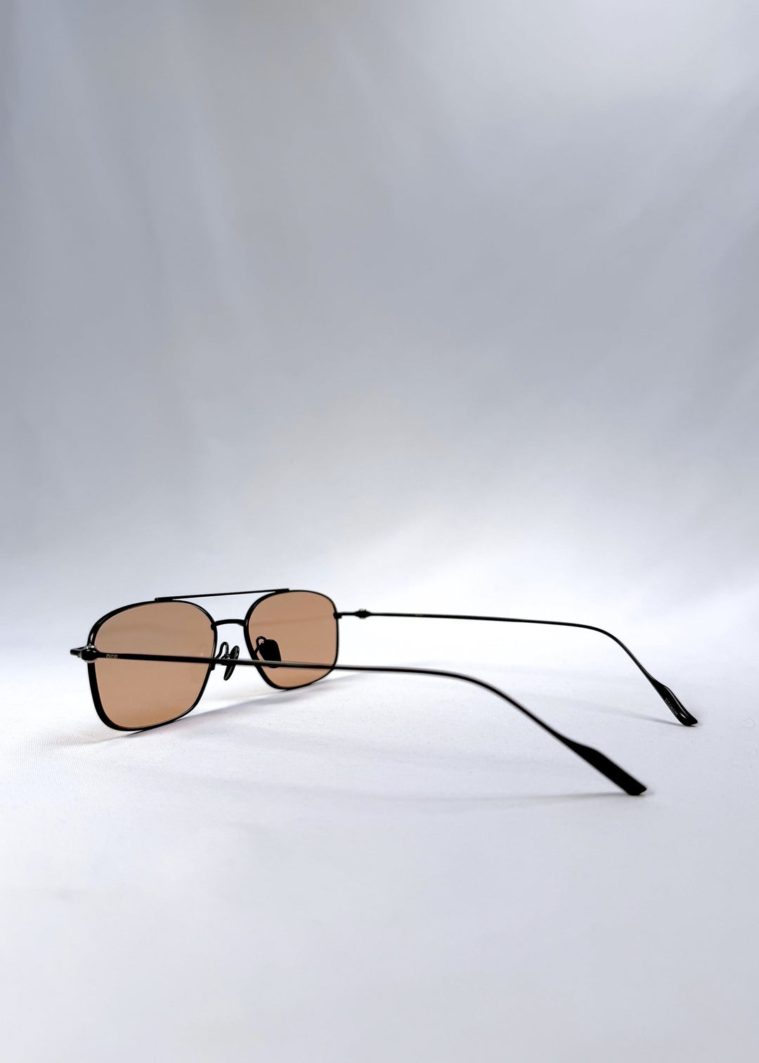 Side-angle view of Seren Arc sunglasses in Obsidian Black, featuring black metal frame and warm brown lenses, showing the lens shape and side temple profile. 