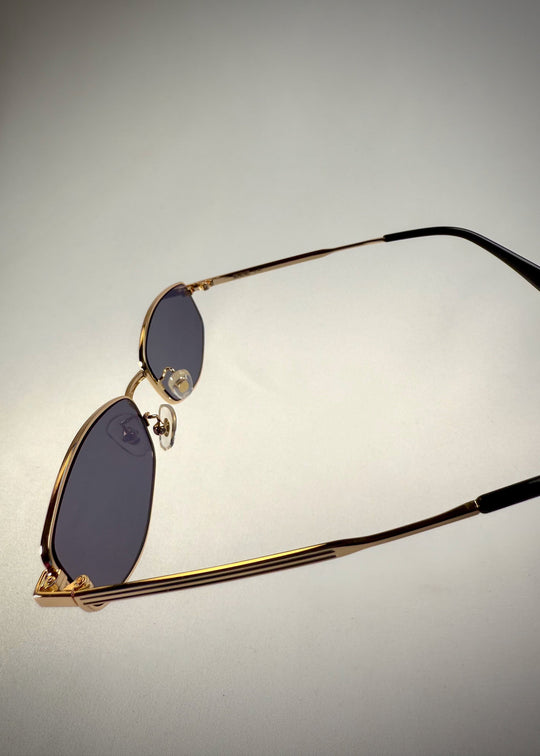Close-up of Sirius B - Gold stainless steel sunglasses, emphasizing the detailed hinge design, blue-gray lenses and polished metal finish. 