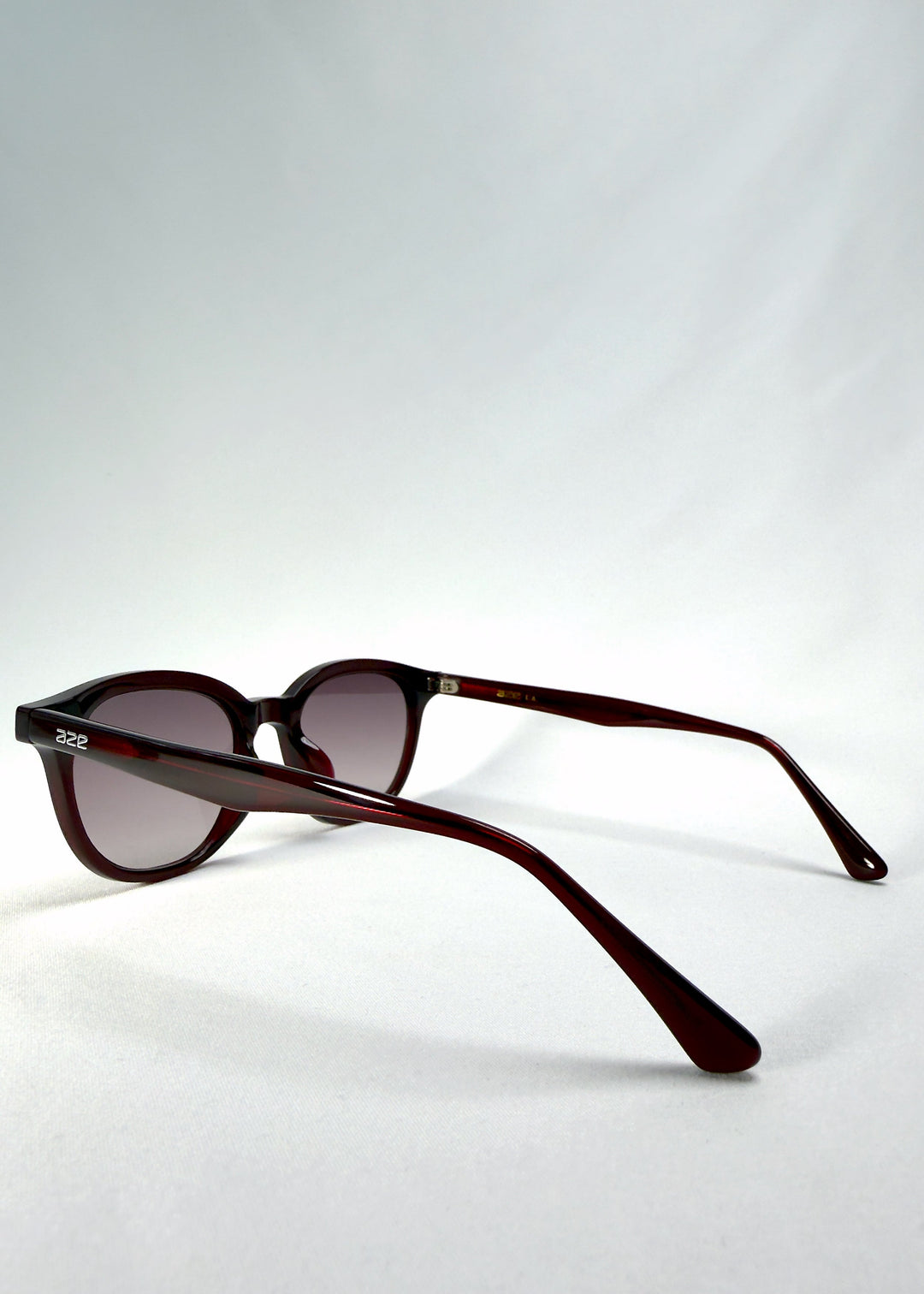 Elvor sunglasses in Mulberry Mist, back-angle view showing the translucent wine-red acetate frame and curved temples. Subtle light reflection highlights the smooth finish. 