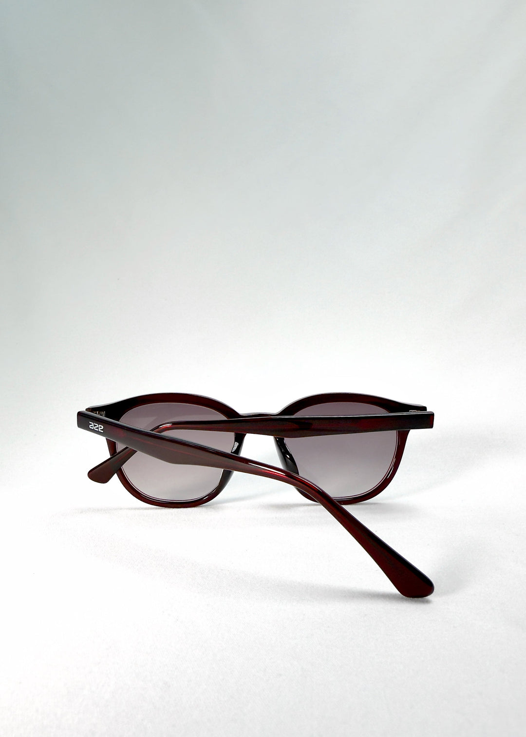 Folded-angle view of Elvor sunglasses in Mulberry Mist showing the slender temples and polished acetate arms in translucent wine red. 