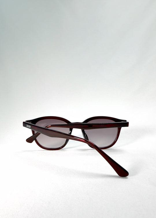 Folded-angle view of Elvor sunglasses in Mulberry Mist showing the slender temples and polished acetate arms in translucent wine red. 