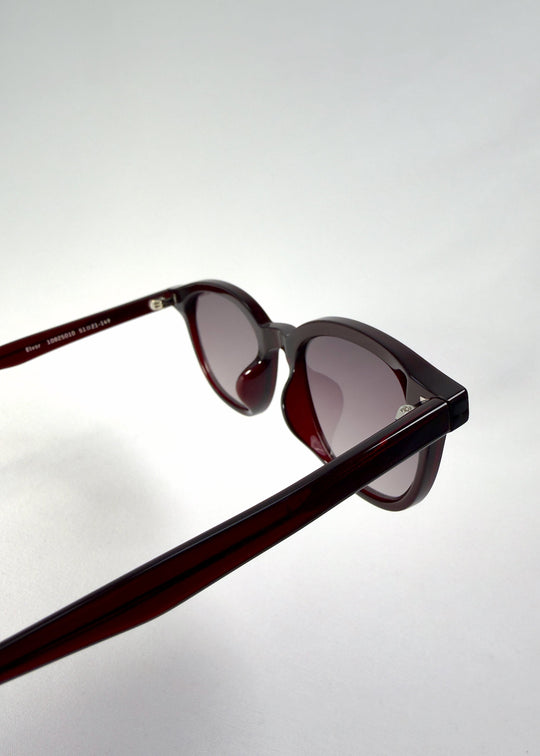 Close-up of Elvor sunglasses in Mulberry Mist focusing on the temple-hinge detail and frosted red acetate texture. Gradient lenses fade from violet to smoky grey. 