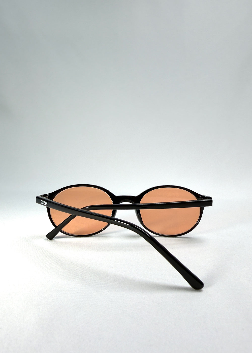 Back-angle view of Glint Softint sunglasses in Obsidian Beam showing slender acetate temples and warm amber lenses.