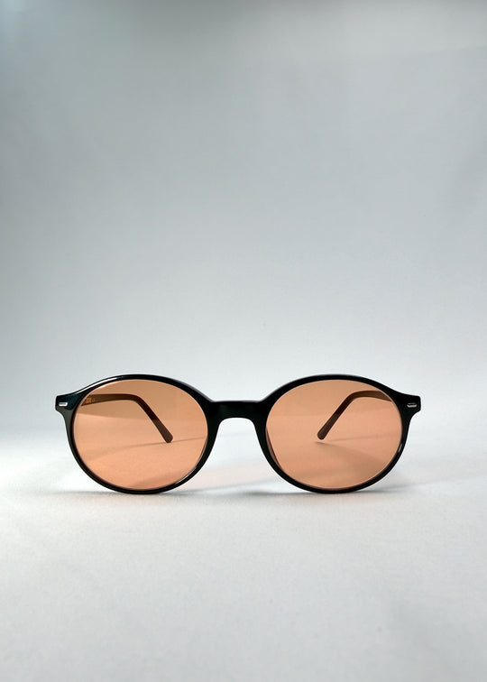 Front view of Glint Softint sunglasses in Obsidian Beam, highlighting the rounded black frame and lightly tinted amber lenses.