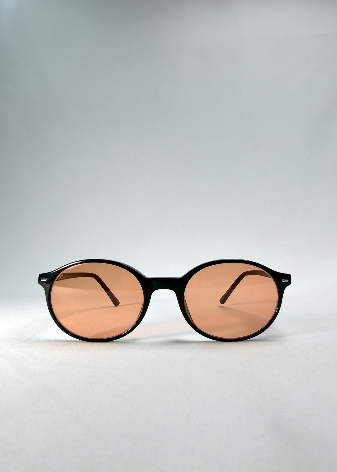 Front view of Glint Softint sunglasses in Obsidian Beam, highlighting the rounded black frame and lightly tinted amber lenses. 