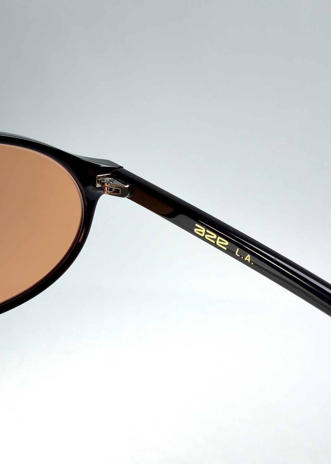 Close-up of Glint Softint sunglasses in Obsidian Beam showing the gold AZE logo on the temple and hinge detail. 