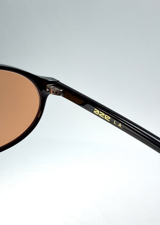 Close-up of Glint Softint sunglasses in Obsidian Beam showing the gold AZE logo on the temple and hinge detail. 