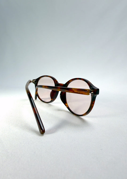 Folded-angle view of Glint Softint sunglasses in Umber Ripple featuring amber-brown acetate temples and light pink Softint lenses.